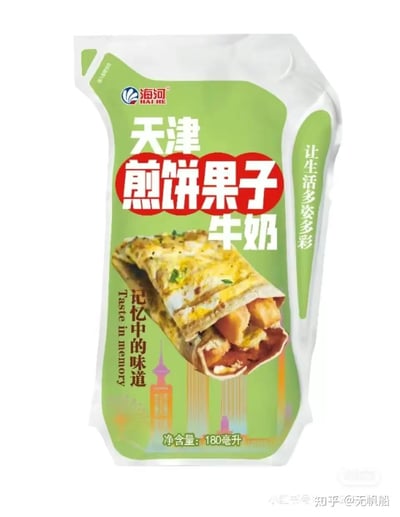 这是天津海河乳业推出的特色风味牛奶——煎饼果子牛奶的产品包装，整体为竖版绿色包装，包装上醒目印有'天津煎饼果子牛奶'字样，搭配天津特色美食煎饼果子的诱人实物图，还加入了天津地标建筑的图案，同时配有'记忆中的味道'、'让生活多姿多彩'的标语，将本地经典早餐美食与牛奶结合，打造充满地域情怀的特色饮品，旨在唤起消费者对天津城市味道的记忆。