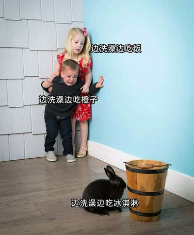 这是一张经过文字改编的真人实拍搞笑梗图，画面呈现室内墙角场景：穿黑色上衣与牛仔裤的小男孩满脸泪水，缩在墙角哭泣，身后穿红色碎花裙的金发小女孩环抱着他，两人均面露惊恐，眼神紧张地看向画面下方的黑色兔子与木质木桶。图中添加了三行递进式的玩梗文字：“边洗澡边吃饭”“边洗澡边吃橙子”“边洗澡边吃冰淇淋”，用越来越离谱的洗澡时的行为，对应小孩看到兔子时的恐惧反应，通过反差感制造搞笑效果，用来调侃生活中那些让人难以接受、觉得离谱的行为。