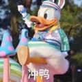 图片中是一只名为“油鸭”的卡通鸭子角色，它身着色彩鲜艳的服饰，手持棒棒糖，面带欢快的表情，站在装饰精美的花车上，整体氛围充满童趣和欢乐。