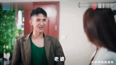 图片中一名穿着棕色夹克内搭绿色背心的男子正微笑着面向一位棕色头发的女子，画面底部显示字幕“老婆”。这是“龙王赘婿”网络广告系列中的经典场景，展现了主角在身份揭露前作为“卑微赘婿”与妻子互动的日常片段，为后续的“打脸逆袭”情节铺垫。