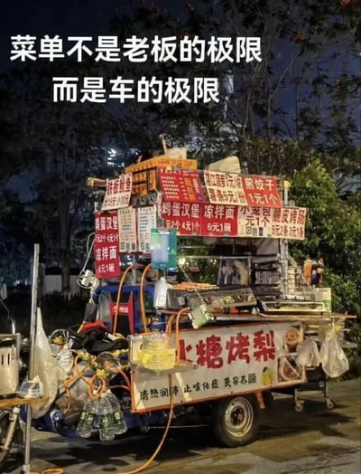 夜间拍摄的街头小吃车照片，车身被各类美食招牌和烹饪设备密集堆满，包括鸡蛋汉堡（2个4元）、凉面（6元1碗）、煎饺子（1元1个）、冰糖烤梨（标注“清热润肺 止咳化痰 美容养颜”）等多种小吃。图片上方配有醒目文字“菜单不是老板的极限 而是车的极限”，以幽默夸张的方式调侃小吃车承载能力已达上限，老板丰富菜单的野心受限于车辆空间。