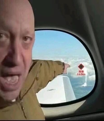 这是一张经过P图改编的恶搞图片，画面中一名光头男子身处飞机客舱内，他表情激动，嘴巴大张，手臂伸出指向飞机舷窗外；舷窗的画面上被添加了标注有“导弹 3.62km”的标识，模拟出飞机即将面临导弹威胁的紧张场景，属于网友制作的玩梗类二次创作内容。