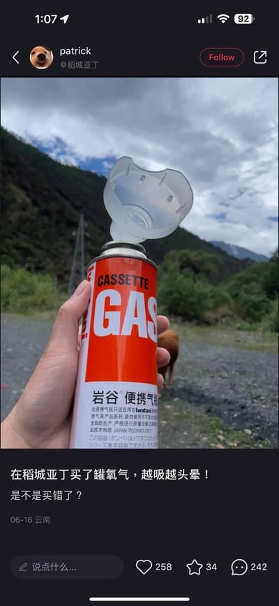 这是一张社交平台的用户动态截图，用户在稻城亚丁旅游时，误将岩谷牌便携卡式炉气罐当作氧气罐购买，使用后感到头晕，于是发布这条动态求助。画面中一只手握着橙白配色的岩谷便携气罐，气罐顶部被套上了一个类似吸氧面罩的透明塑料罩，背景是稻城亚丁户外的山地与多云天空，远处还能看到一头棕色的牲畜。动态配文为“在稻城亚丁买了罐氧气，越吸越头晕！是不是买错了？”，下方标注发布时间为06-16，发布地为云南，同时显示该动态获得258个点赞、34个收藏、242条评论。这条内容的核心笑点是用户的生活乌龙，将燃气罐误认为氧气罐，引发网友调侃。