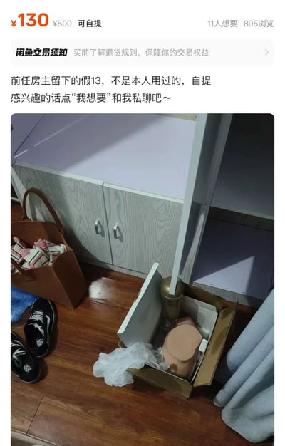 该图片为闲鱼平台的二手商品 listing 截图，展示了一款标注为“假13”（假iPhone 13）的商品出售信息。截图上方显示价格为¥130（原价¥500），支持自提，已有11人想要、895次浏览。商品描述提到“前任房主留下的假13，不是本人用过的，自提”，并引导感兴趣者点击“我想要”私聊。图片下方包含一张实物照片，显示一个纸箱内装有疑似手机的物品，放置在木地板上，周围有黑色鞋子、棕色手提袋等物品。