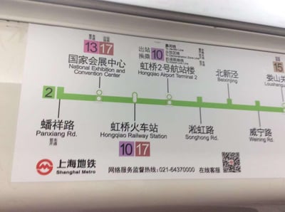 这是一张实拍的上海地铁2号线车厢内线路导视牌，展示了蟠祥路、国家会展中心、虹桥火车站、虹桥2号航站楼、北新泾、威宁路及娄山关（部分）站点。导视牌标注了各站点的换乘信息：蟠祥路暂未开通；国家会展中心可换乘暂未开通的13、17号线；虹桥火车站可换乘10、17号线；虹桥2号航站楼可换乘10号线，还标注了可换乘暂未开通的嘉闵线、示范区线、机场联络线；娄山关站可换乘15号线。导视牌底部配有上海地铁标识、服务监督热线021-64370000以及在线客服二维码，整体信息清晰，为乘客提供出行换乘指引。
