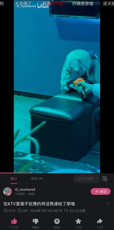 这是B站用户i0_nowhere4发布的搞笑视频截图，画面呈现KTV场景：一只手拿着话筒递向放置在沙发凳上的初音未来玩偶，上方弹幕有“太会唱了”“我靠我气笑了”“的确是原唱”等内容。视频标题和画面玩了趣味梗——初音未来作为众多VOCALOID歌曲的虚拟原唱，在KTV场景下被“递话筒”，制造出让原唱唱歌的搞笑反差感。该视频发布于2024年1月14日，播放量达67万，点赞17.2万，评论959条，有23人正在观看，属于结合现实场景与虚拟IP的趣味创作。