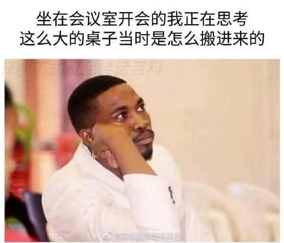 这是一张文字加注的真人表情包，图中黑人男子手肘支撑，手托脸颊，眼神放空看向一侧，呈现出若有所思、心不在焉的状态。上方配文“坐在会议室开会的我正在思考这么大的桌子当时是怎么搬进来的”，精准还原了很多人开会时思绪飘到无关小事上的走神状态，内容搞笑且容易引发职场人士的共鸣，没有双关、谐音梗等特殊设定。