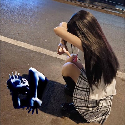 夜晚的街道上，一名长发女孩蹲坐在柏油路面上，她穿着白色无袖上衣和黑白格子短裙，黑色长袜搭配厚底鞋。女孩将双臂交叉放在膝盖上，头部埋在臂弯中，只露出部分侧脸和长长的黑发。她伸出一只手，食指指向地面上一个蓝色的、类似抽象生物的影子形象。这个影子有着类似爪子的形状和扭曲的面部轮廓，与女孩形成互动姿态。背景中可以看到湿润的路面反射着灯光，路边有停放的车辆和人行道边缘，营造出一种神秘又略带梦幻的夜晚氛围。