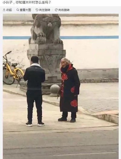 这是一张结合动漫与现实的趣味梗图，画面为现实街头场景：一位白发大爷身着带有红色祥云纹样的黑色长袍，造型高度还原日本动漫《火影忍者》中的角色自来也，他正面向一位背对镜头的年轻男子，似乎在向对方询问。图片顶部添加了配文“小伙子，你知道木叶村怎么走吗？”。
木叶村是《火影忍者》中主角漩涡鸣人所在的木叶隐村，大爷的cos造型加上这句问路的话，制造出打破次元壁的搞笑效果，让熟悉《火影忍者》的观众感受到现实与动漫结合的趣味，属于火影迷的整活创作。