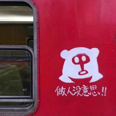 这是一张实拍的红色列车车厢照片，车厢外壁上有一处白色手绘涂鸦：一个有着小熊轮廓的原创卡通形象，脸部用红色画出抽象化的五官，整体神态蔫蔫的、无精打采；形象下方配有白色手写字体‘做人没意思!!’，直白地传递出消极、倦怠的情绪。画面左侧可见列车的车窗，窗内隐约能看到车厢内的座椅，整体场景充满了生活化的情绪宣泄感。