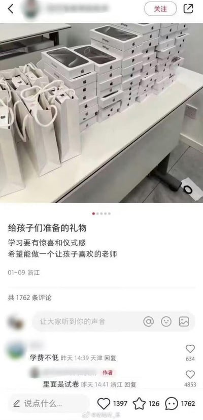 这是一张社交媒体截图，分为上下两部分：上方是一张堆满苹果手机包装盒和白色手提袋的桌子，营造出要送苹果手机当礼物的假象；下方是发布者的配文和评论区。发布者配文称“给孩子们准备的礼物 学习要有惊喜和仪式感 希望能做一个让孩子喜欢的老师”，定位浙江，发布时间01-09。评论区有网友调侃“学费不低”，发布者回复“里面是试卷”，形成强烈反差，制造出搞笑效果。
反差梗说明：用昂贵的苹果手机包装盒作为噱头，实际里面是试卷，利用学生和网友的预期落差制造笑点。