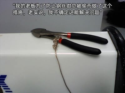 图片展示了一把放置在白色台面上的钢丝钳，老板为了防止它被偷，用一根细铁丝将钢丝钳的钳身捆绑起来并固定在台面上。上方的配文是员工的吐槽，指出这个防盗措施完全无效——因为用来固定的细铁丝可以被这把钢丝钳轻松剪断，根本无法阻止钢丝钳被偷走，属于典型的迷惑且无效的职场操作，充满了讽刺感。
