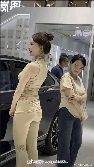 这是一张汽车展厅的实拍竖屏图，画面中两位女性站在启源品牌展车旁，形成强烈视觉反差：左侧女性穿着修身米色套装，发型精致，姿态优雅；右侧女性穿着宽松T恤和牛仔裤，双臂交叉，表情嫌弃又无奈地看向一侧，这种穿搭与神态的反差感成为图中笑点。
