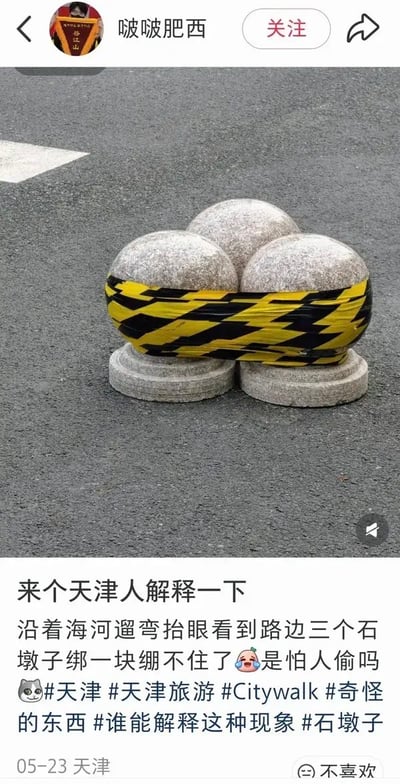 这是一张竖屏社交媒体截图。上方显示用户名“啵啵肥西”、关注按钮和分享按钮；中间照片拍摄于沥青路面上，三个灰色花岗岩球形挡车石墩被凑成一簇，中部被黄黑斜纹警示胶带横向缠绕，看起来像是被绑在一起，下方可见两个圆形石质底座。下方配文称“来个天津人解释一下”，并说自己沿着海河遛弯时看到三个石墩子绑在一块，调侃“绷不住了”“是怕人偷吗”。图中的趣味点在于“绑一块”和“绷不住了”形成语义双关：字面上是胶带把石球捆住，网络语中“绷不住”则表示忍不住笑或情绪失控。从画面判断，这更可能是临时安全或维护处理：石球可能被移动、松动或待维修，用胶带把三者缠成较稳定的一簇，防止滚动并提醒路人注意；黄黑胶带本身很薄，并不具备真正防盗功能，因此“怕人偷”应是发帖人的玩笑说法。