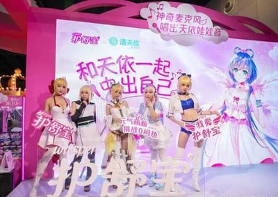 这是一张护舒宝与虚拟歌手洛天依合作的线下推广活动现场照片，整体以粉色为主色调，营造出活泼可爱的二次元氛围。画面中有五位身着cosplay服装的真人女性，她们站在活动舞台上，各自手持带有品牌宣传语的牌子，分别为“护舒宝”“元气萌新 挑战0闷热”“我爱护舒宝”，姿态活泼，面带微笑，配合活动进行展示。背景的大型宣传板上印有洛天依的卡通形象，还有“护舒宝 × 洛天依”的合作标识，以及宣传语“和天依一起 中出自己”，结合护舒宝的品牌调性与活动主题，此处“中出”疑似为“活出”的排版失误或谐音错误，应为宣传女性活出自我的理念；同时板上还有“神奇麦克风 唱出天依娃娃音”的趣味标语，突出活动的互动性与趣味性。画面底部印有“护舒宝 whisper”的品牌标识，整体场景是品牌借助二次元IP进行的线下营销活动，旨在吸引年轻消费群体关注产品，传递产品舒适、贴合年轻群体需求的特点。