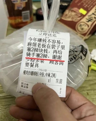 这是一张手持外卖订单小票的实拍图，小票来自南宁的栗记螺蛳粉门店，订单内容为一份售价19.88元的中份中辣瘦肉炒螺蛳粉，配送费0元，餐盒费2元。顾客在备注栏先写下了非常离谱的玩笑式要求：“今年赚钱不容易，麻烦老板在袋子里塞200块钱，再给骑手塞200，谢谢”，这段内容被红笔划掉，下方是真实的用餐需求：“少粉多菜 顾客需要餐具”。整图通过离谱要求和真实需求的强烈反差制造搞笑效果，以戏谑的方式调侃当下赚钱难的情绪，没有双关、谐音梗等特殊表意。