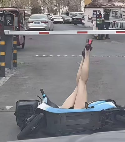 一张停车场场景的搞笑图片，画面中央的栏杆下方，一辆蓝色 scooter 疑似倒地，车身上伸出一双穿着红色高跟鞋的女性腿部，呈现出夸张的悬空姿势。背景中可以看到停放的多辆汽车和路边的建筑物，整体构图营造出一种荒诞又滑稽的视觉效果。