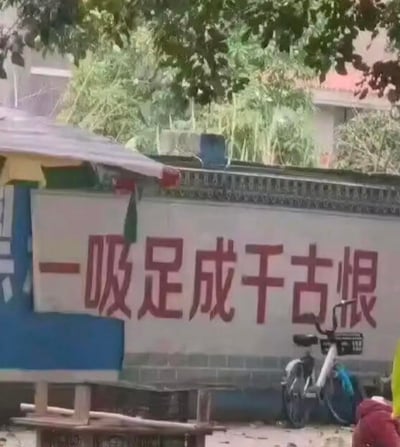这是一张户外实景拍摄的图片，画面中的墙面上绘制着一条禁毒宣传标语，内容为“一吸足成千古恨”。该标语明显改编自经典俗语“一失足成千古恨”，但出现了用字错误，将“失”误写为“足”，形成了乌龙感十足的宣传内容。画面里还能看到停在墙边的自行车、简易棚子以及背景的树木，呈现出乡村或城郊的户外场景。
该标语属于禁毒宣传的失误创作，错字改编经典俗语，让原本严肃的宣传内容变得滑稽可笑。