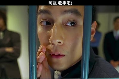 这是一张流行网络表情包，画面截取自香港电影《新警察故事》的片段，吴彦祖饰演的反派关祖（阿祖）被关在蓝色铁栏杆之后，右手抬至脸颊旁，面部带有汗珠，眼神向画面左侧瞟，神态很有张力，图片顶部配有白色文字“阿祖 收手吧！”，常被网友用来调侃劝说他人停止上头、整活或者做出冒险行为。