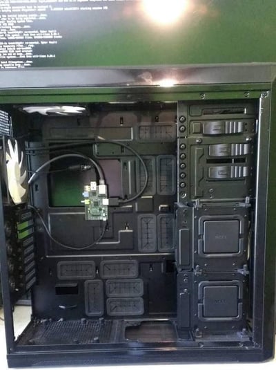 这张图片展示了一台打开侧面板的黑色NZXT品牌电脑机箱，机箱内部尚未安装主板、CPU、显卡等核心计算硬件，仅保留了机箱自带的前置风扇、多层硬盘支架等基础结构。在机箱背部的理线区域，固定着一块带有接口和连接线的小型外接电路板，属于额外加装的扩展部件。机箱右侧的硬盘支架上印有NZXT品牌标识，背部预留了多个理线孔位和硬件安装空间，整体呈现出待组装或进行硬件改装的状态。图片上方还显示了一段英文系统日志类文本，内容涉及Intel网卡的相关信息。
