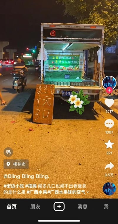 柳州夜晚的街头，一辆本应售卖水果鲜花的卡车摊位前立着一块手写木牌，上面赫然写着“卖空气 十元 3口”，反差感拉满。卡车车厢内亮着灯，隐约可见水果陈列，上方招牌写着“水果鲜花姐姐 生活越过越有钱”。背景中有机动车和行人路过，街道旁有树木和路灯，充满生活气息。图片带有社交媒体平台界面元素，显示地点“柳州市”，作者“@Bling Bling Bling.”，以及点赞3717、评论1087、收藏221的数据，配文 hashtags 包括#街边小吃 #摆摊 等，调侃“闻多几口也闻不出老板卖的是什么果”，用“广西水果味的空气”玩梗，幽默又接地气。