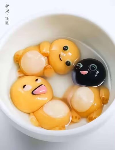 这是一张AI生成的创意节日图片，将热门卡通IP《奶龙》中的角色奶龙及其伙伴，设计成了汤圆的形态，四个造型各异的“汤圆”泡在碗中的清水中：一个微笑的黄色奶龙侧躺在水中，一个吐舌搞怪的奶龙仰躺，还有一个好奇呆萌的黑色小形象，以及一个仅露出身体的奶龙，整体造型软萌可爱，充满了元宵节的趣味氛围，没有双关或谐音梗。