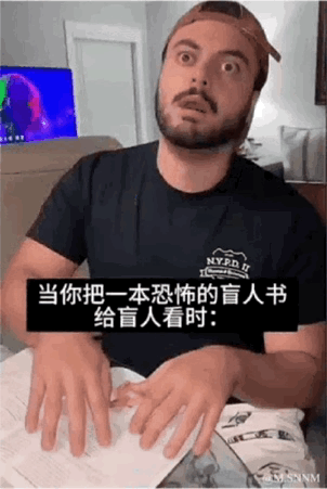 这是一段动态GIF梗图，画面中一名真人男性瞪大双眼，满脸惊恐，双手在面前的纸张上做出触摸盲文的动作。图中配有字幕“当你把一本恐怖的盲人书给盲人看时：”，用夸张的表演模拟盲人触摸到恐怖盲文内容时的惊恐反应，通过无厘头的设定制造搞笑效果。