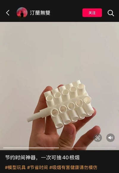 图片展示了一只手握着一个白色塑料装置，该装置有多个管状结构，看起来像是某种可以同时容纳多根香烟的器具。图片下方配有文字“节约时间神器，一次可抽40根烟”，并带有#模型玩具 #节省时间 #吸烟有害健康请勿模仿等标签。这张图片以幽默夸张的方式展示了一个虚构的“吸烟神器”，实际上是在讽刺这种不健康且不切实际的“时间节约”方式，同时通过最后的标签传达了吸烟有害健康的警示。