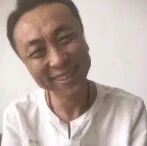 图片中是一位穿着白色上衣的男性，他面带明显夸张的笑容，眼睛微眯，嘴角上扬幅度较大，表情看起来有些滑稽有趣，背景为纯色，突出人物面部表情。