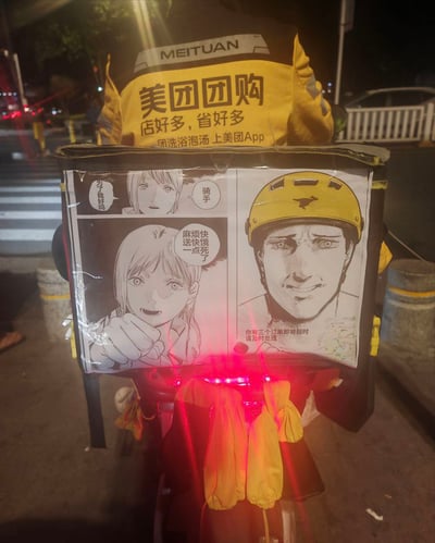 夜晚街头，一名美团骑手的背影特写。骑手穿着印有“美团团购 店好多，省好多 团洗浴泡汤上美团App”字样的黄色工装，背后的外卖箱上贴有黑白手绘风格漫画。漫画分多格，左侧女生角色配文“为了钱好吗”“麻烦快点送快饿死了”，右侧骑手戴黄色头盔，表情无奈，下方文字提示“你有三个订单即将超时 请及时处理”。画面通过漫画与现实结合，幽默展现了外卖骑手面临顾客催单和订单超时的日常压力场景。