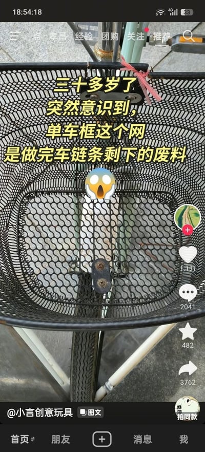 这是一张抖音平台的图文内容截图，画面主体为黑色金属网材质的自行车前置车筐的特写，车筐的波浪形网格纹理与自行车链条的纹理高度相似；画面上方叠加黄色配文“三十多岁了 突然意识到，单车框这个网 是做完车链条剩下的废料”，配文下方还有一个双手捂脸的惊讶表情emoji；截图保留了抖音的完整界面元素，右侧显示该内容获1.1万点赞、2041条评论、482次收藏、3762次转发，底部是抖音的功能导航栏，左下角标注了内容发布者为@小言创意玩具。