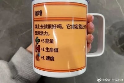 这是一张原始拍摄的静态单图，画面中一只手握着白色马克杯的杯柄，杯子表面印有橙底的图文内容，将日常的咖啡类比为RPG游戏中的增益物品：以“咖啡”为名称，配文“闻上去就很好喝。它肯定能让你充满活力。”，还列出了类似游戏属性的加成效果：+3能量、+1生命值、+1速度，用游戏化的设定调侃咖啡能提神醒脑、补充精力的作用，充满趣味性，属于创意文创产品。