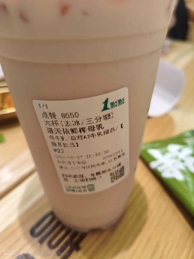 这是一张消费者实拍的一点点奶茶出餐杯照片，杯身的点单标签出现了多处明显的打印错误，将原本的“鲜榨椰乳”误写为“鲜榨母乳”，还有其他文字排版和内容错误，整体场景因为商家的失误显得十分荒诞搞笑，很有槽点。
标签存在多处文字打印失误：“鲜榨椰乳”被错误打印为“鲜榨母乳”，属于输入错误造成的荒诞效果，引发网友吐槽。