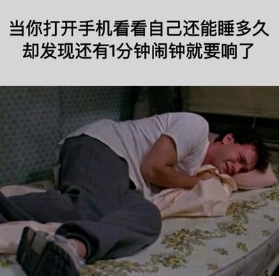 图片上半部分为文字：‘当你打开手机看看自己还能睡多久却发现还有1分钟闹钟就要响了’，下半部分是一名男子躺在床上的场景。男子穿着白色T恤和深色裤子，身体蜷缩，抱着枕头，面部表情痛苦，似乎因即将响起的闹钟而感到极度无奈和绝望，生动展现了人们面对起床闹钟时的崩溃瞬间。