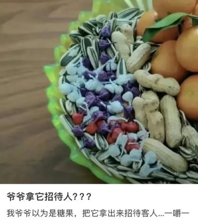 这是一张顶配底文的静态单图，画面上方是一个绿色花边果盘，果盘里摆放着带叶的橘子、带壳花生、葵花籽，还有一堆色彩丰富、包装样式类似糖果的物品，这些物品实际是宠物驱虫药；画面下方配有两行文字，第一行是“爷爷拿它招待客人？？？”，第二行是“我爷爷以为是糖果，把它拿出来招待客人...一嚼一”，完整讲述了爷爷误将外观像糖果的驱虫药认成真正的糖果，摆进果盘用来招待客人的搞笑乌龙事件，充满了生活中的荒诞感和趣味性，正是因为驱虫药和糖果外观高度相似，才导致了这个误会的发生。