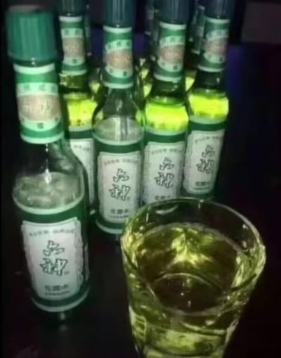 图中摆放着多瓶六神花露水，前方的玻璃杯中倒入了类似花露水的液体，模仿酒局拼酒的场景，用日常驱蚊的花露水恶搞硬核喝酒的画面，制造出强烈的反差感，充满荒诞搞笑的整活趣味。