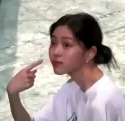 这张图片是一张静态截图，主体是艺人欧阳娜娜，她穿着白色短袖上衣，头发低扎成马尾，眼神睁大，面露惊讶又带着疑惑的神情，同时抬起右手，用食指指向自己的脸部区域。画面整体带有一点模糊感，这个表情和手势组合起来，传递出疑惑、惊讶或者不敢置信的情绪，常被制作成表情包，在社交媒体上用来表达类似的心情，比如对某件事感到意外、疑惑不解时使用。