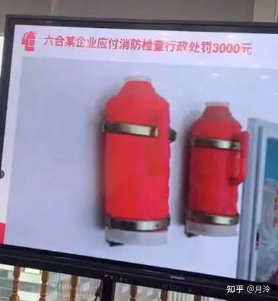 这张图片展示的是一张PPT通报现场，两只红色热水瓶被装在墙上假装成灭火器，企图通过消防检查，结果被罚款3000元。图片上方有红色标题，说明事件背景，下方标明出处。“热水瓶当灭火器”属于极为离谱的行为，画面给人荒诞和无语感，常用于表达现实生活中的离谱应付和敷衍了事。

特别说明：有明显的谐音和视觉双关——热水瓶和灭火器同为红色，用于视觉欺骗，应对检查，属于典型的“以假乱真”/“能省就省”操作。