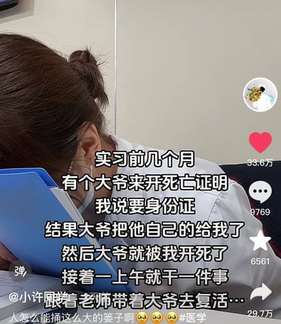 图片展示了一位穿着白大褂的实习医生低头趴在蓝色文件夹上的场景，配文讲述了一个实习期间的搞笑乌龙事件：有位大爷来开死亡证明，医生索要身份证时大爷递了自己的，结果误开了大爷的死亡证明，整个上午都在跟着老师带大爷去"复活"。