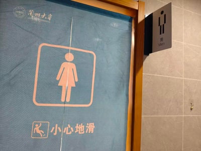 这张照片拍摄于兰州大学校园内的一处卫生间，门帘上印有粉色的女性卫生间标识、“小心地滑”的提示语，左上角还有兰州大学的校徽与校名；但门侧的墙面上却悬挂着男性卫生间的标识牌，两种标识形成明显矛盾，呈现出有趣的设施标识乌龙场景。