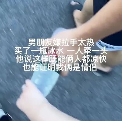 图片展示了一对情侣的创意牵手方式。由于天气炎热，男朋友嫌直接拉手太热，于是买了一瓶冰水，两人各牵瓶子的一头。图片上方配有文字说明这一有趣场景，体现了情侣间的幽默和夏日的小智慧。