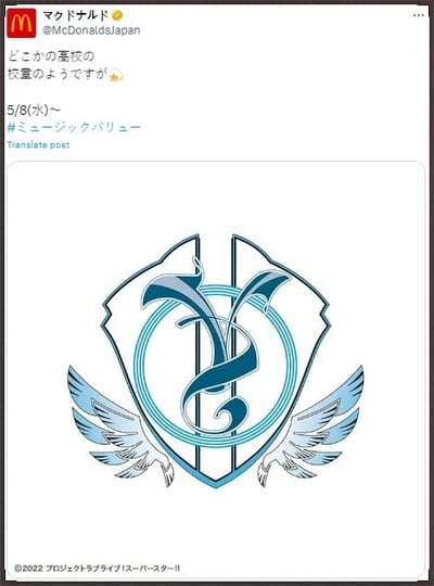 这是日本麦当劳官方X（原推特）账号发布的联动预热内容，推文配文称“看起来像是某个高中的校徽✨”，并预告5月8日（周三）开始的相关活动，附带话题标签#ミュージックバリュー。配图是一枚带有翅膀的盾牌造型徽章，内部有独特艺术化符号，底部标注了《LoveLive!Superstar!!》的版权信息，表明这是与该偶像企划的联动宣传，用模仿日本高中校徽的设计来吸引粉丝关注即将开启的活动。