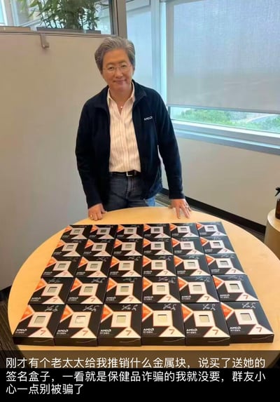 图中是AMD公司CEO苏姿丰（Lisa Su），她身着带有AMD标识的外套，站在摆满签名版AMD锐龙7 CPU包装盒的圆桌后方，面带微笑，双手搭在桌边。图片下方配有恶搞文字：“刚才有个老太太给我推销什么金属块，说买了送她的签名盒子，一看就是保健品诈骗的我就没要，群友小心一点别被骗了”。该梗图通过将苏姿丰的形象调侃为推销保健品的老太太，把高端CPU戏谑成“金属块”，利用身份和物品的反差制造出搞笑的效果，在电脑硬件爱好者圈子中流传。