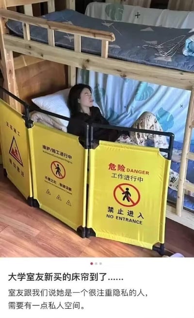 这是一张大学宿舍场景的实拍图，下铺的大学室友为了获得私人空间，把原本用于施工警示的黄色可折叠围挡当成床帘围在了自己的床边。围挡上印有各种醒目的施工警示标语：“正在施工 请勿靠近”、“维护/施工进行中”、“危险 DANGER 工作进行中 禁止进入”等，配文提到室友表示自己很注重隐私，需要私人空间，这种独特的“床帘”方式用拒绝进入的警示标语来隔绝外界打扰，硬核又搞笑，创意拉满。