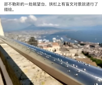 图片展示了那不勒斯一处眺望台的实景，前景为带有盲文凸点的金属扶栏，背景是模糊的城市全景，可见密集建筑群、远处水域及山脉，天空中有少量云朵。图片上方配有文字说明扶栏盲文用于描绘景致，体现对视觉障碍人士的关怀，通过触觉帮助其感受风景。