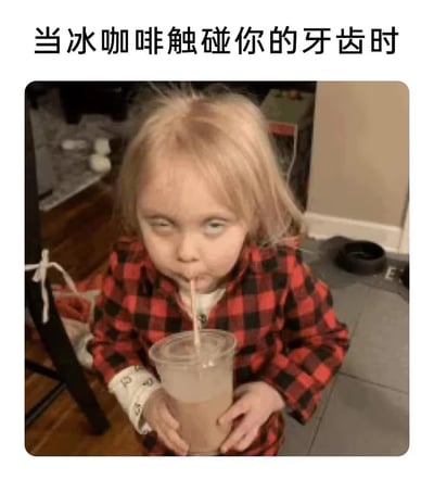 图片上方配有文字“当冰咖啡触碰你的牙齿时”，下方是一名金发儿童穿着红黑格子衣物，手持透明吸管杯正低头喝饮料，表情夸张迷离，生动展现了冰咖啡接触牙齿时那种又刺激又上头的搞笑瞬间。