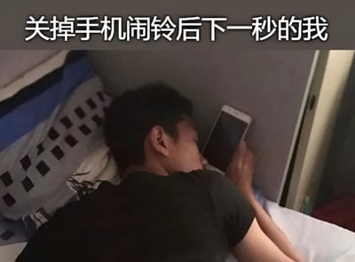 图片展示了一个人在关掉手机闹钟后立刻又陷入沉睡的场景。图中人物躺在床上，闭着眼睛，一只手拿着手机，似乎刚刚关掉闹铃就立刻进入了睡眠状态，完美诠释了许多人早晨起床时的真实状态。