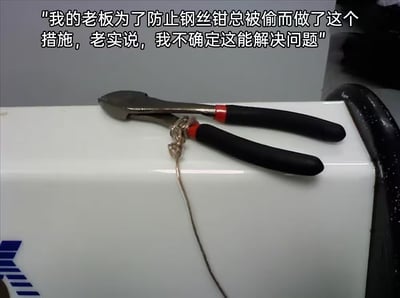 图片展示了一个具有讽刺意味的场景：一把黑色手柄带红色装饰的钢丝钳被用一根细绳子简单地绑在一个白色物体上。图片上方配有文字说明："我的老板为了防止钢丝钳总被偷而做了这个措施，老实说，我不确定这能解决问题"。这张图片的幽默之处在于用钢丝钳（一种切割工具）本身被一根脆弱的绳子保护，形成了一种逻辑上的矛盾和无效防护的滑稽感。