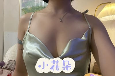 图片展示了一位女性的上半身特写，她穿着一件浅绿色缎面吊带，领口呈深V形。脖子上戴着一条精致的项链，吊坠小巧闪亮。左臂上部有一处纹身，图案细节不清晰。背景中可以看到墙上挂着一幅风景画和一盏带有黄色灯罩的台灯。图片底部中央有一个云朵形状的文字框，里面写着蓝色的“小花朵”三个字。整体画面呈现出一种优雅、柔和的氛围。