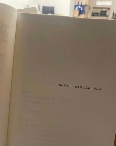 这是一张实体书内页的实拍图片，页面底色为浅米色，在页面偏右下位置印有一行黑色献词：“本书献给每一个想要实实在在工作的人”。画面左侧能看到相邻书页的边缘，上面有模糊的浅色字样，背景是虚化的室内环境，整体聚焦于这行传递职场正向态度的献词，明确了书籍的受众是渴望踏实工作的职场人群。